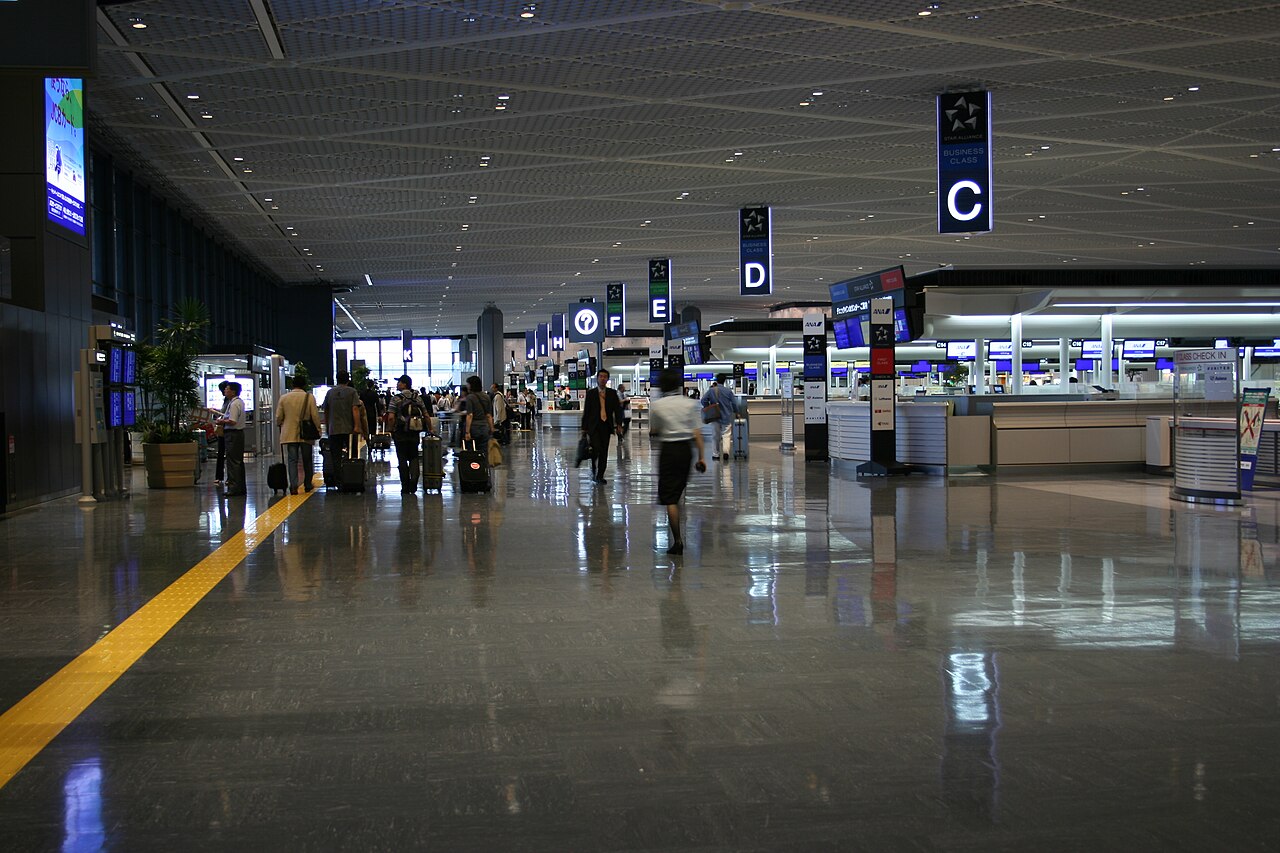 The international departure floor at Narita Airport Terminal 1, travellers walking towards the check-in counters with suitcases.
